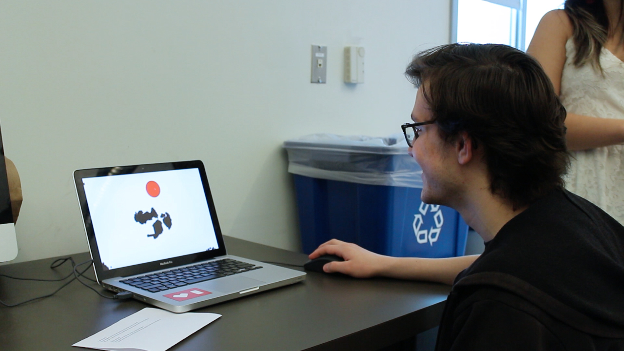 View full size version of a person using a mouse to interact with a laptop that has a red circle and black blobs on the screen